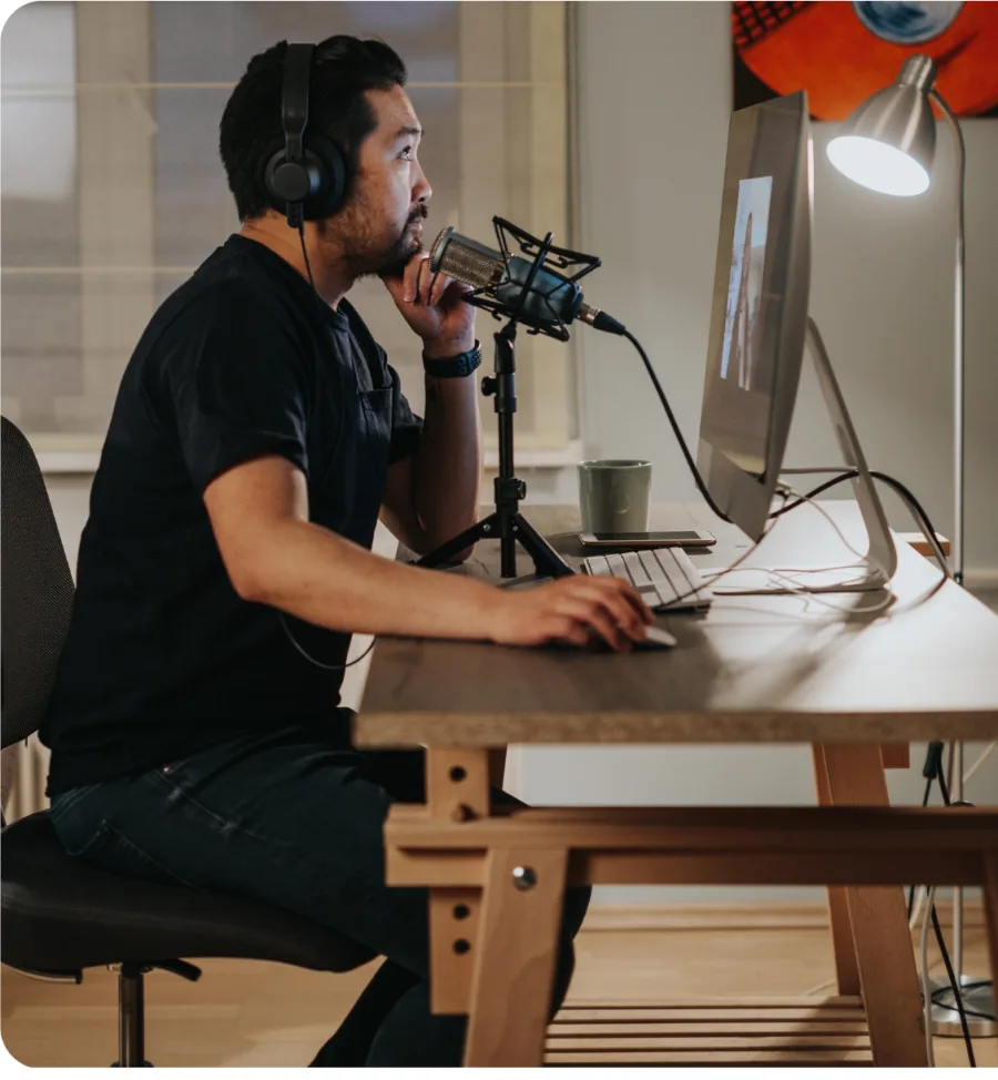 Ein Mann mit Kopfhörern spricht am Schreibtisch in ein Podcast-Mikrofon